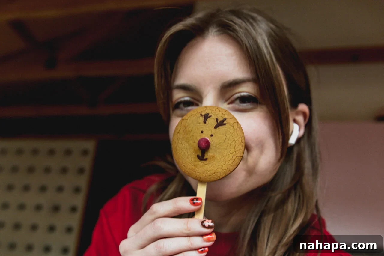 A person joyfully holding up a decorated gingerbread Rudolph reindeer cookie to their face, ready to enjoy the festive treat.