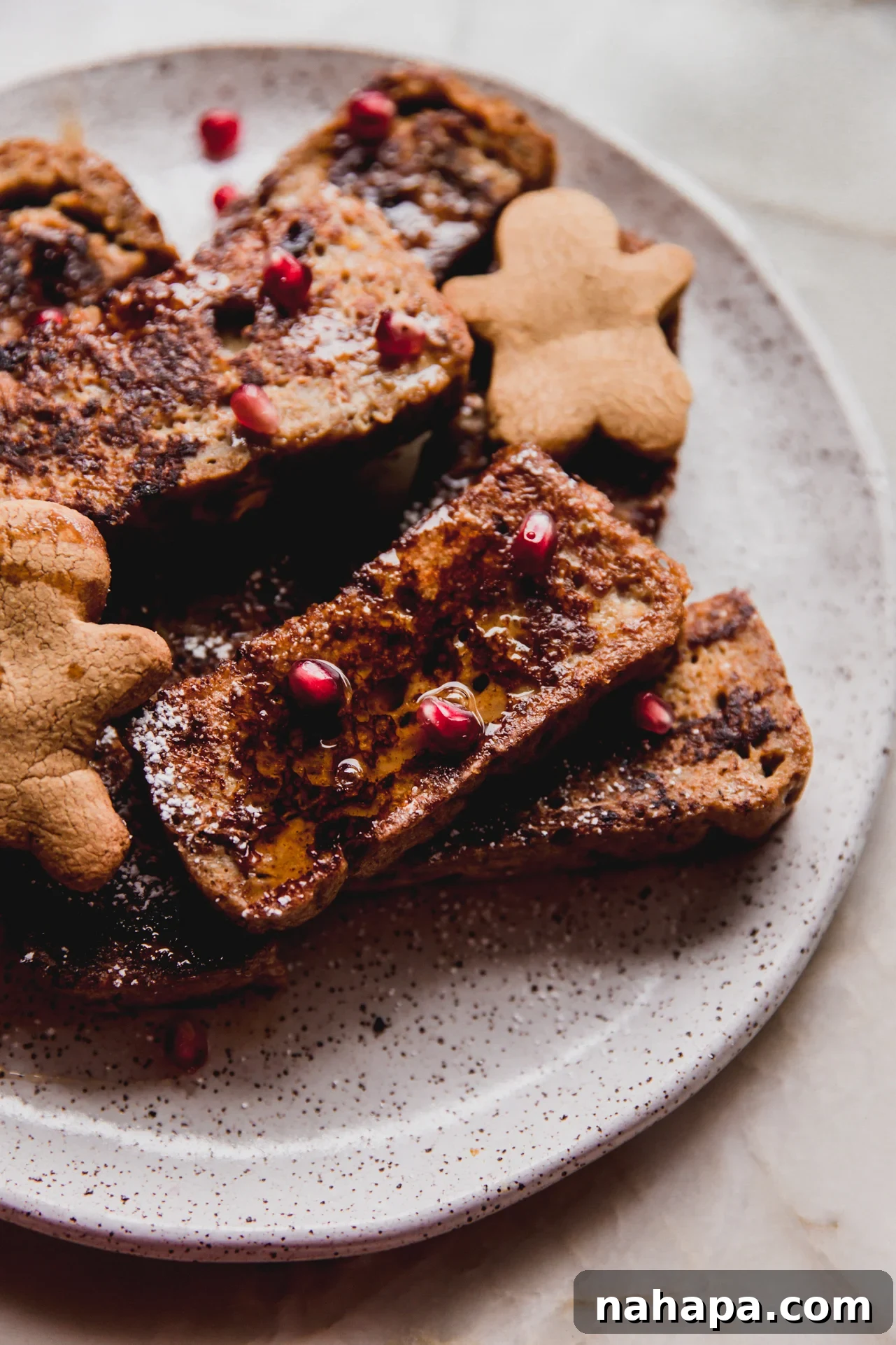 Gluten free gingerbread french toast on a plate topped with pomegrante seeds and maple syrup.