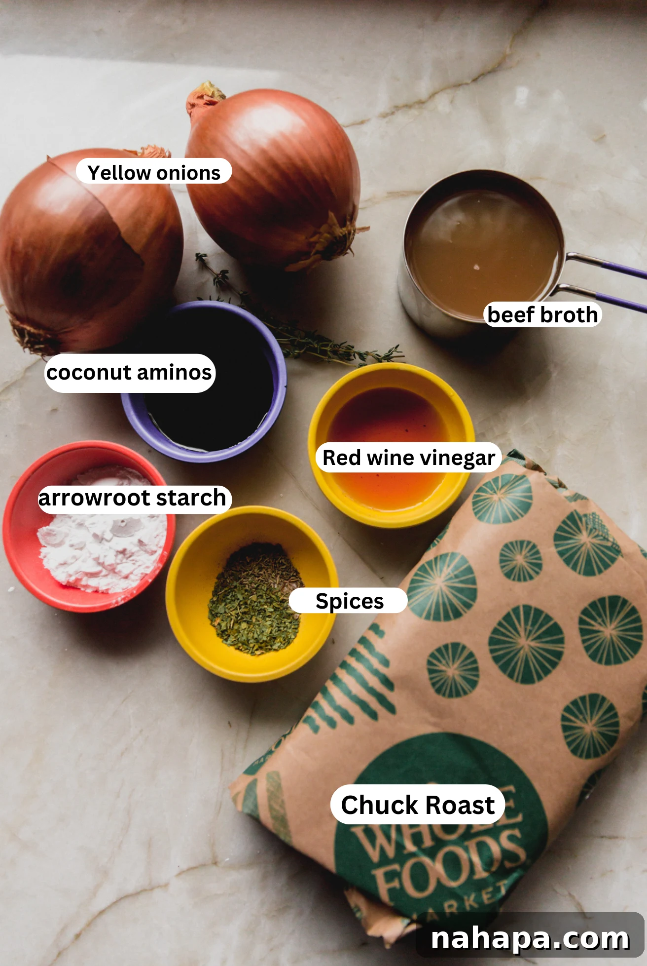 French Onion Braised Beef 3 All the essential ingredients neatly laid out for preparing French onion pot roast, including chuck roast, yellow onions, beef broth, coconut aminos, red wine vinegar, and various herbs and seasonings.