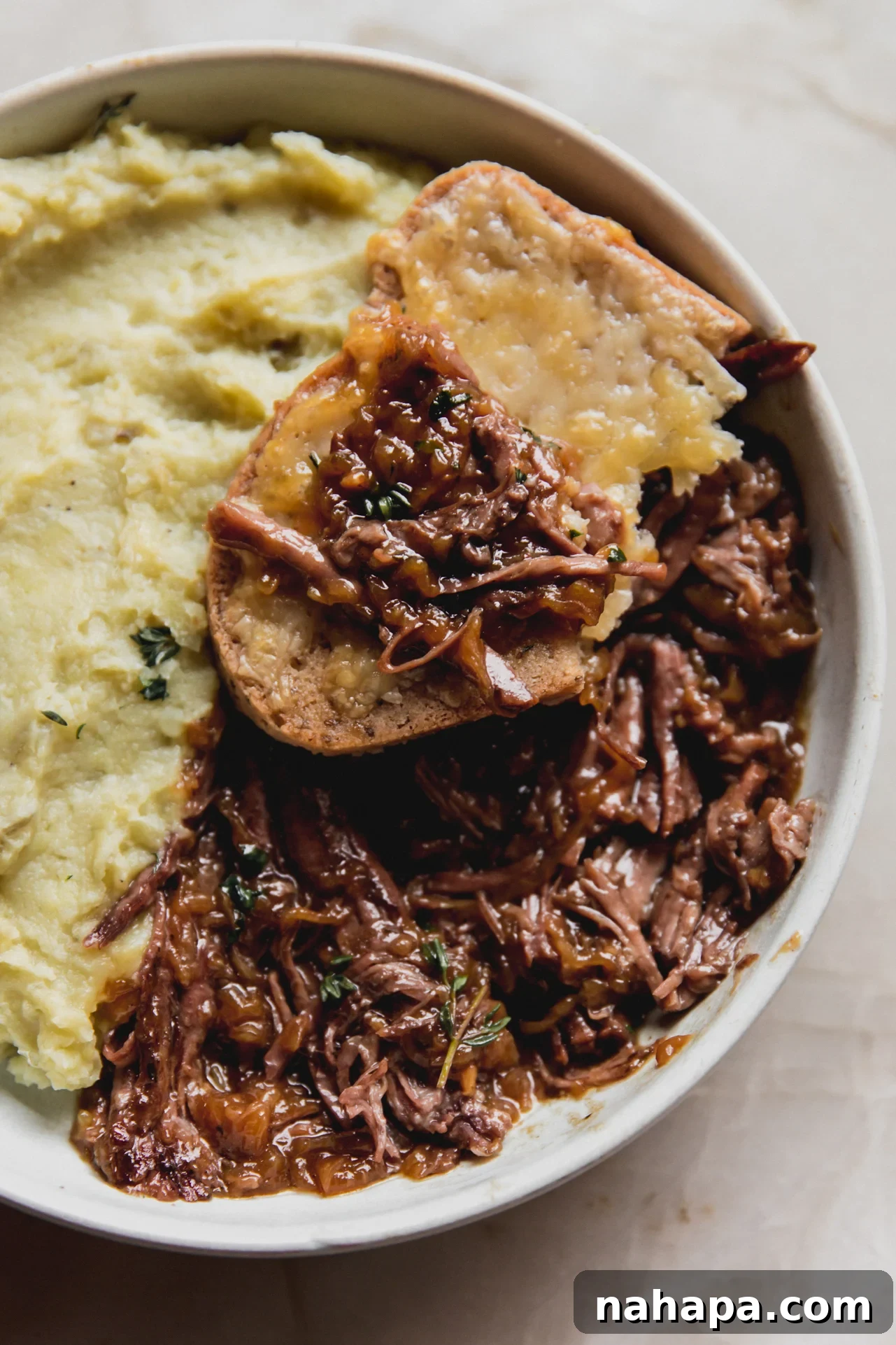 French Onion Braised Beef 4 A close-up of tender French onion pot roast served in a bowl, with a piece of cheesy toast resting on the side, ready for dipping.