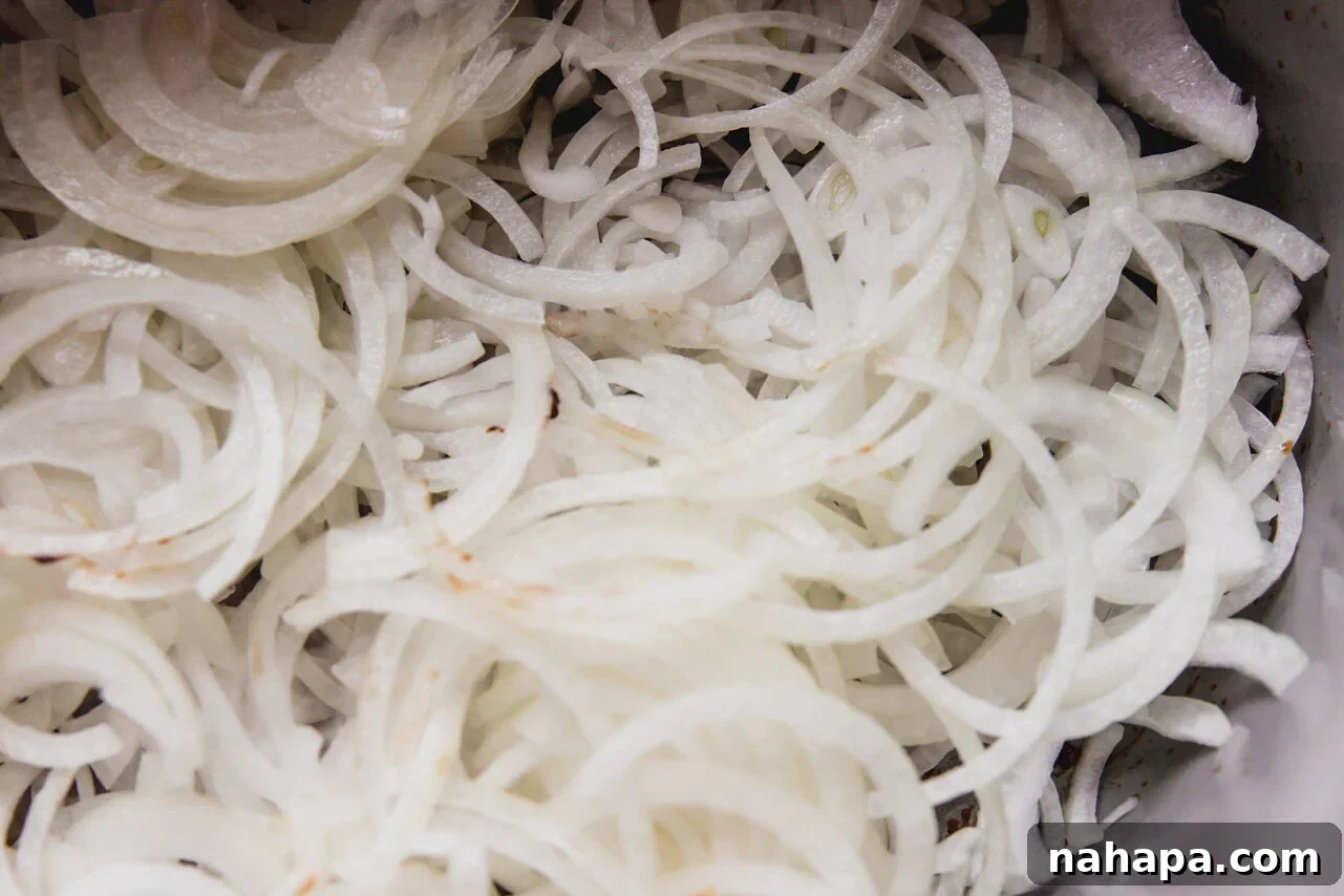 French Onion Braised Beef 7 Thinly sliced yellow onions resting in the bottom of a Dutch oven before being cooked, ready to begin the caramelization process.