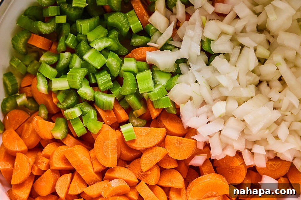 Finely chopped yellow onion, celery, and carrots in a large pot, ready to be sautéed for the soup base.