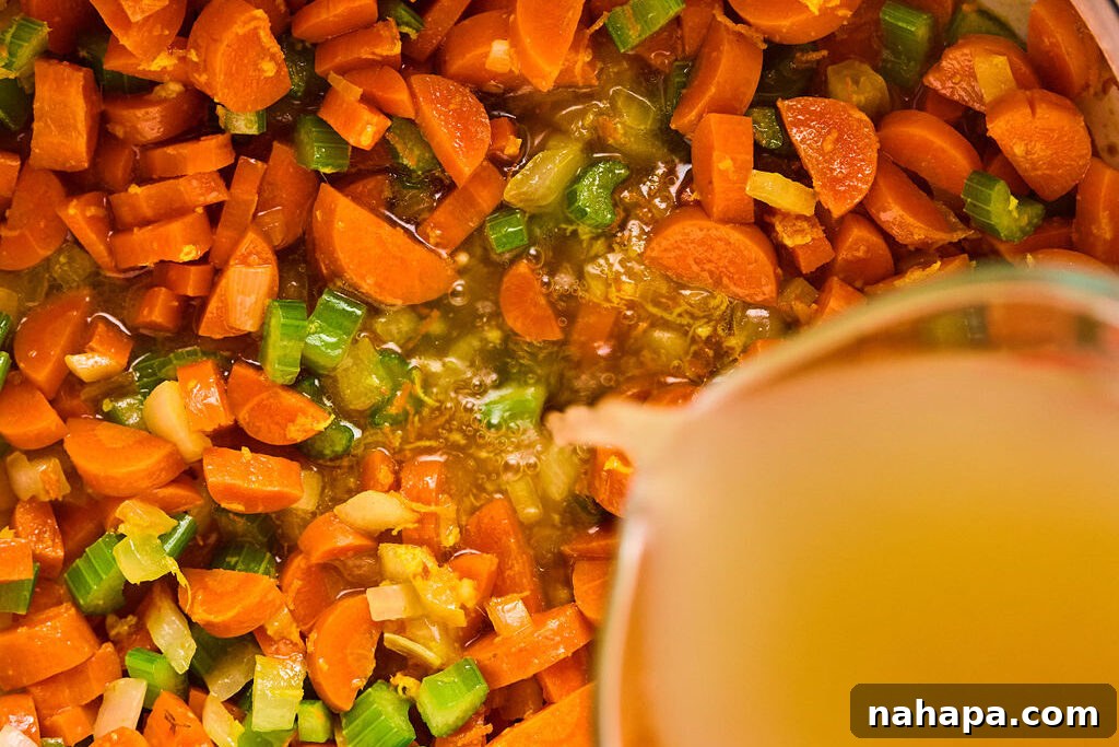 Rich chicken broth being poured into the pot with sautéed vegetables and spices, ready to simmer and create a flavorful soup.