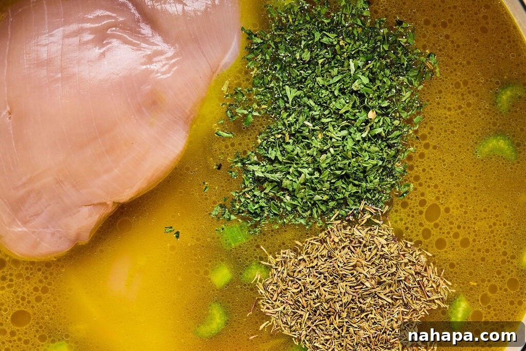 Raw boneless chicken breast submerged in the simmering broth with vegetables and herbs, ready to cook through.