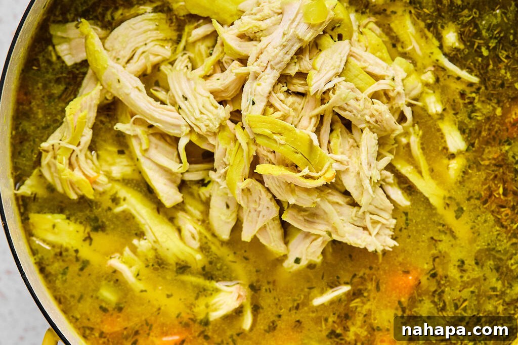 Shredded chicken on a cutting board, ready to be returned to the pot of soup after the pasta has cooked.