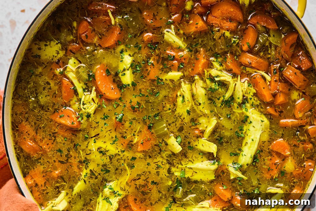 A freshly prepared bowl of Lemon Turmeric Chicken Noodle Soup, garnished with a sprinkle of fresh chopped parsley and a lemon slice.