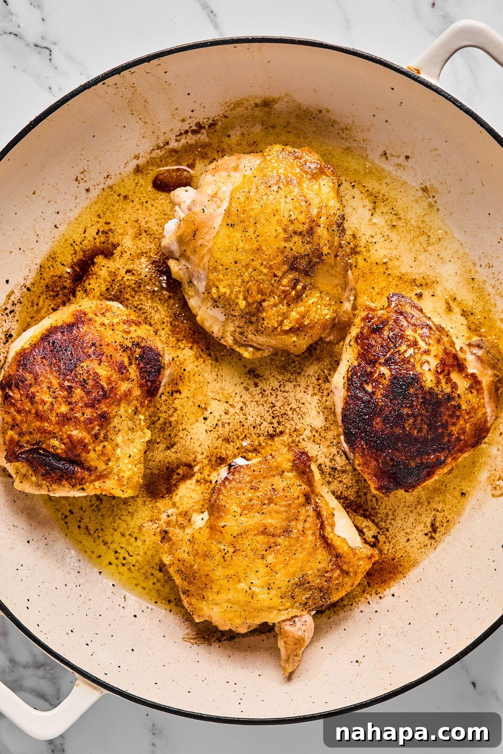 Crispy chicken thighs resting on a plate after being seared, showcasing their golden-brown skin.