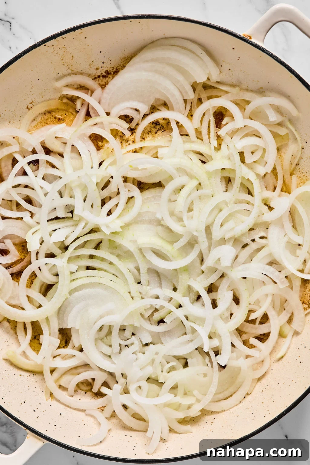 Thinly sliced yellow onions added to the same pan where the chicken was seared, ready to be sautéed.