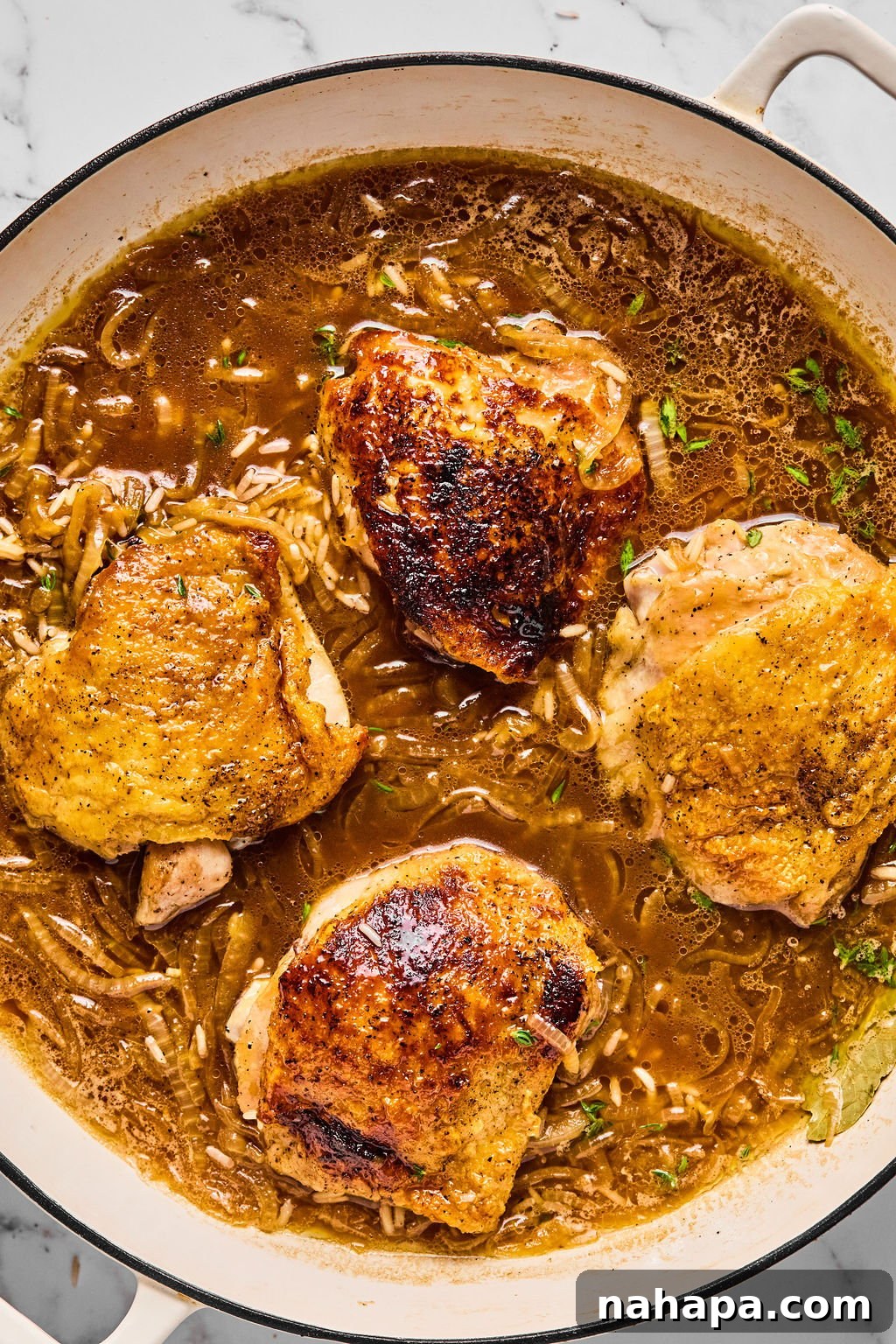 Seared chicken thighs arranged back in the pan with the rice and onion mixture, before baking.