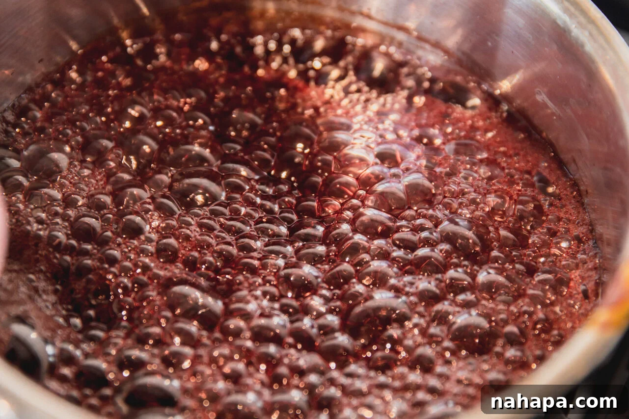 Elderberry syrup and honey gently simmering in a saucepan on the stove, beginning to transform into a lollipop mixture.