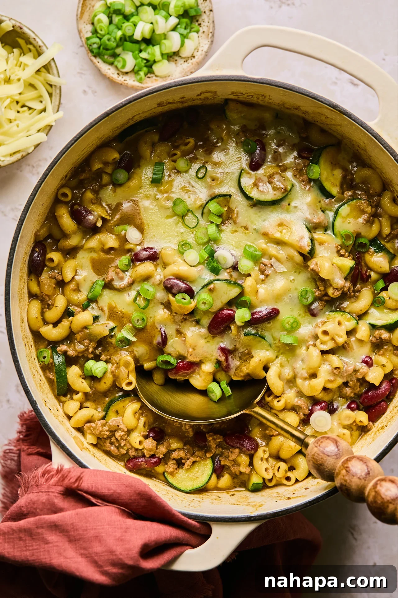 Gluten free chili mac topped with cheese in a cast iron pot, with a spoon.