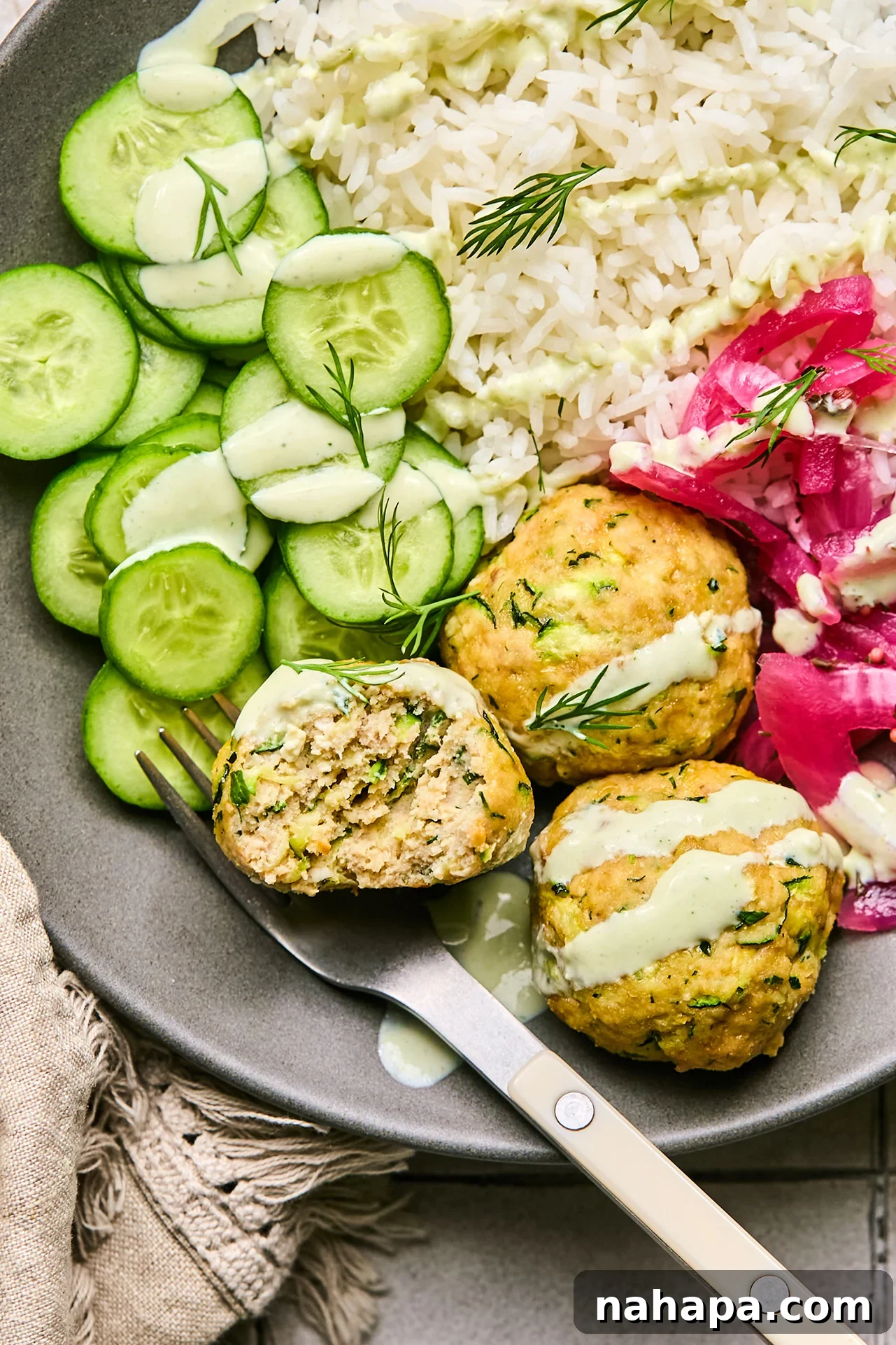 Zesty Gluten-Free Turkey Feta Bites 10 A vibrant bowl of turkey feta meatballs, garnished with fresh cucumber, fluffy rice, and tangy pickled onions, all generously topped with creamy yogurt sauce – a complete and delicious meal.