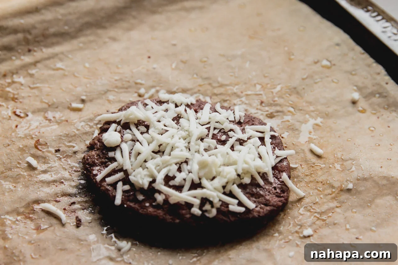 Cooked burger topped with shredded cheese.