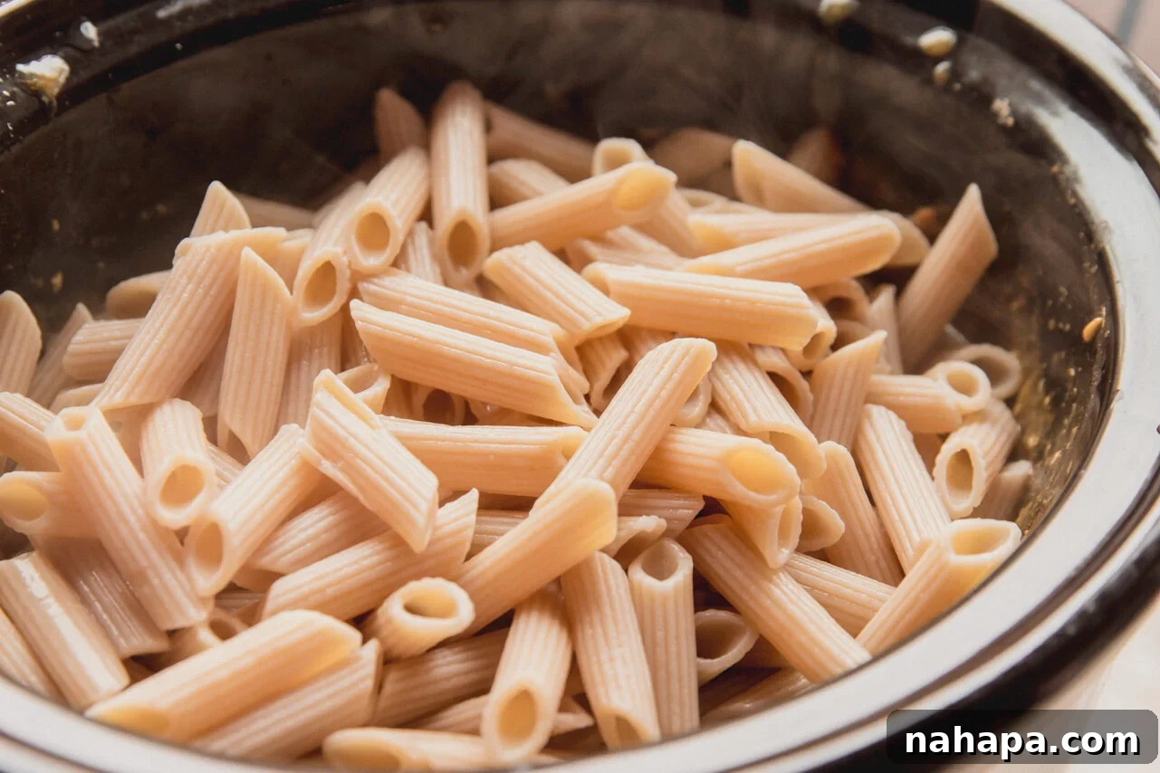 Velvety Slow Cooker Chicken Pasta 6 Perfectly cooked gluten-free pasta added to the creamy shredded chicken sauce in the slow cooker, ready to be combined.