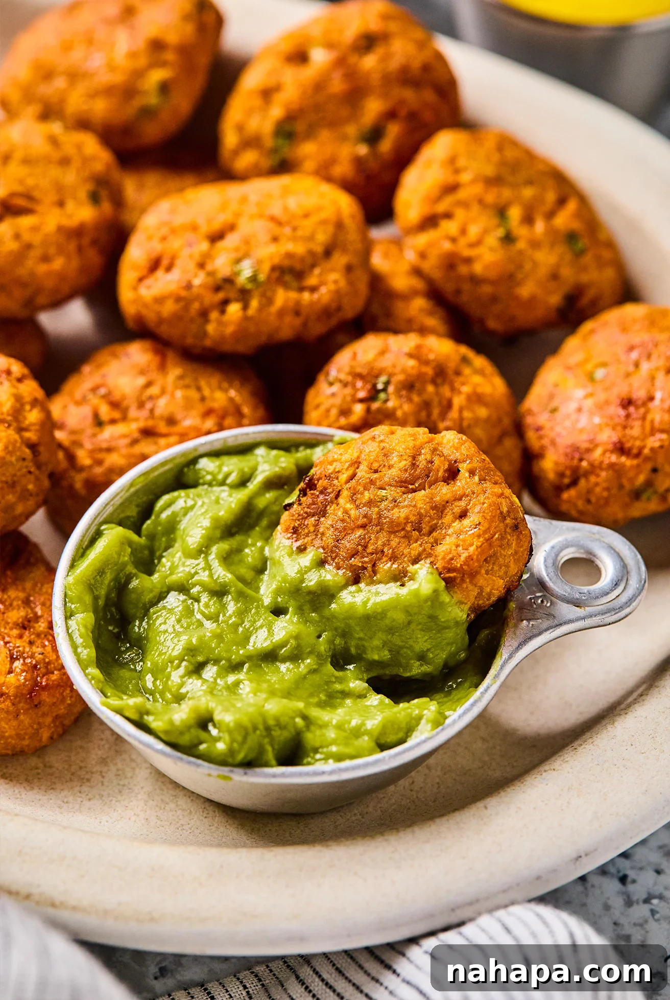 Sweet potato chicken poppers on a plate with one dipping into a bowl of guacamole. 