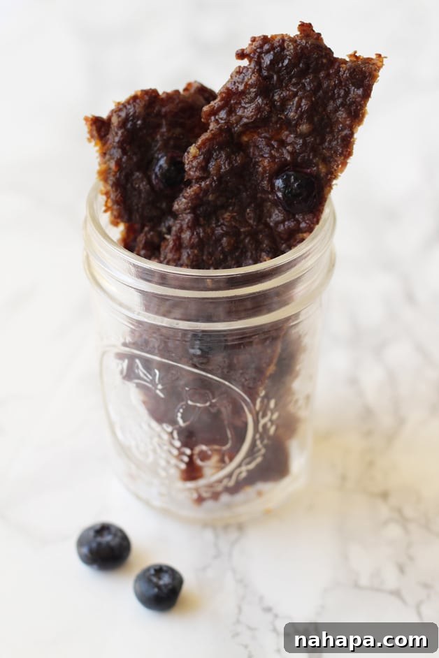 A glass jar filled with perfectly dried homemade blueberry beef jerky pieces, ready for snacking.