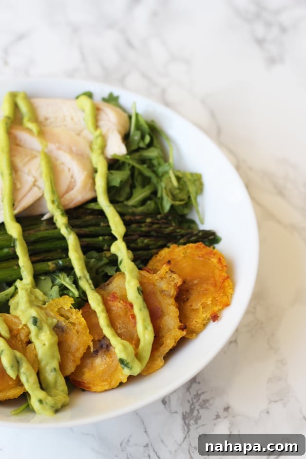 A bowl filled with fried plantains, chicken, aspargus, greens and topped with dressing.