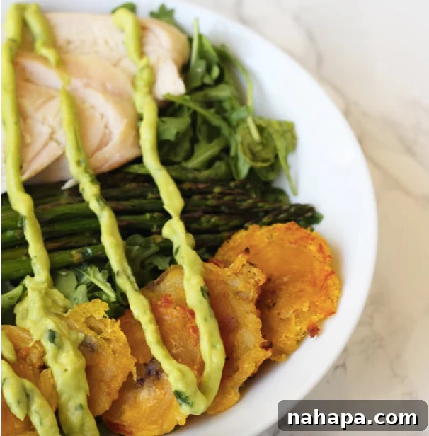 A bowl filled with fried plantains, chicken, aspargus, greens and topped with dressing.