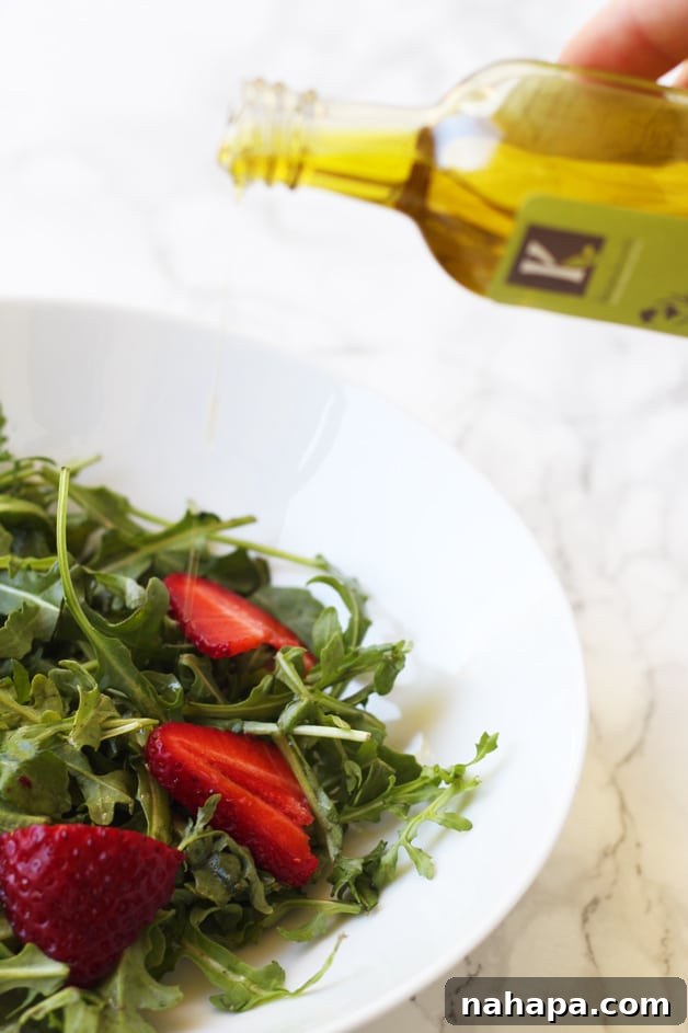 High-quality olive oil being poured from a bottle onto a fresh, vibrant salad.
