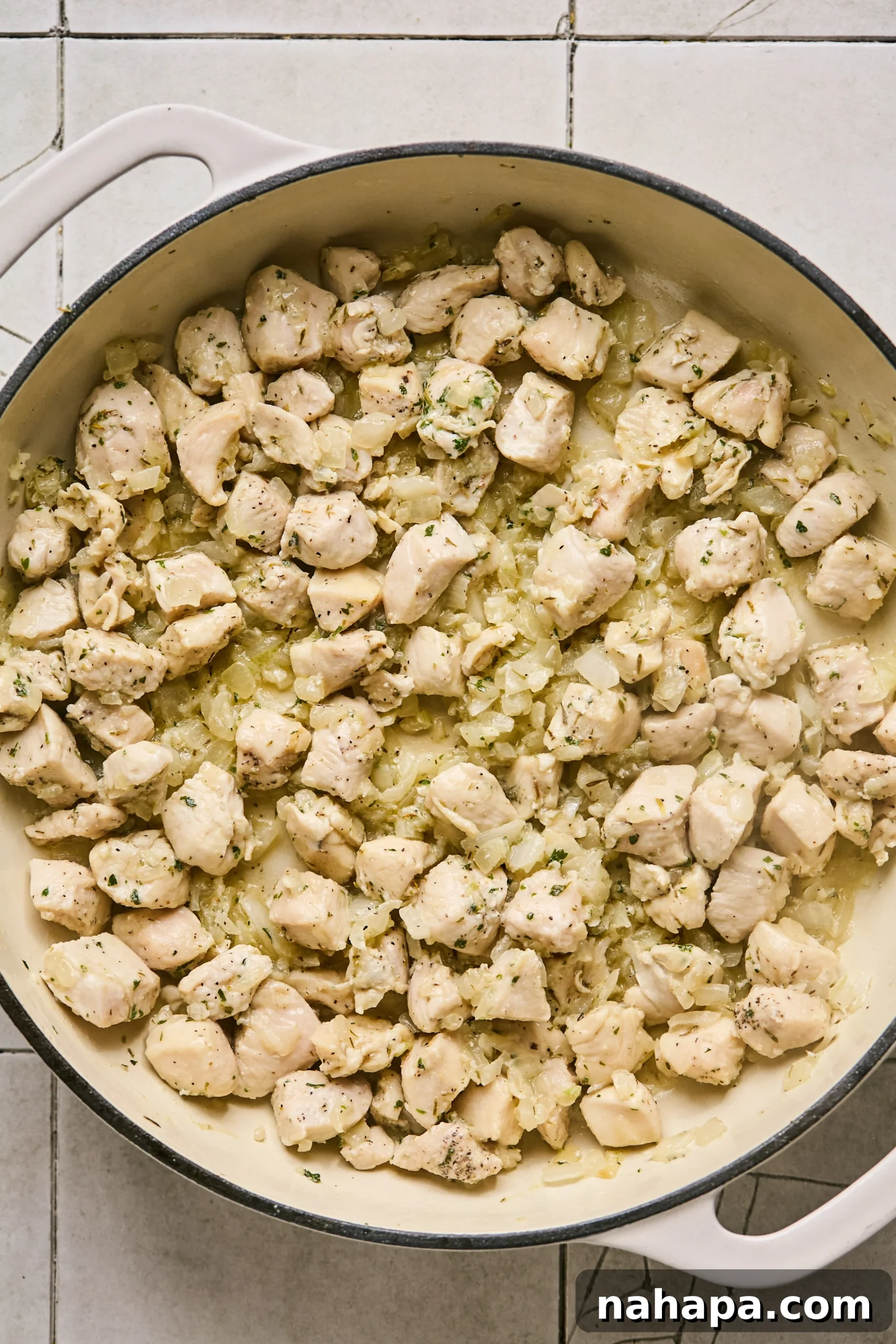 Cubed chicken breast added to the pan with sautéed onions and garlic, beginning to brown.