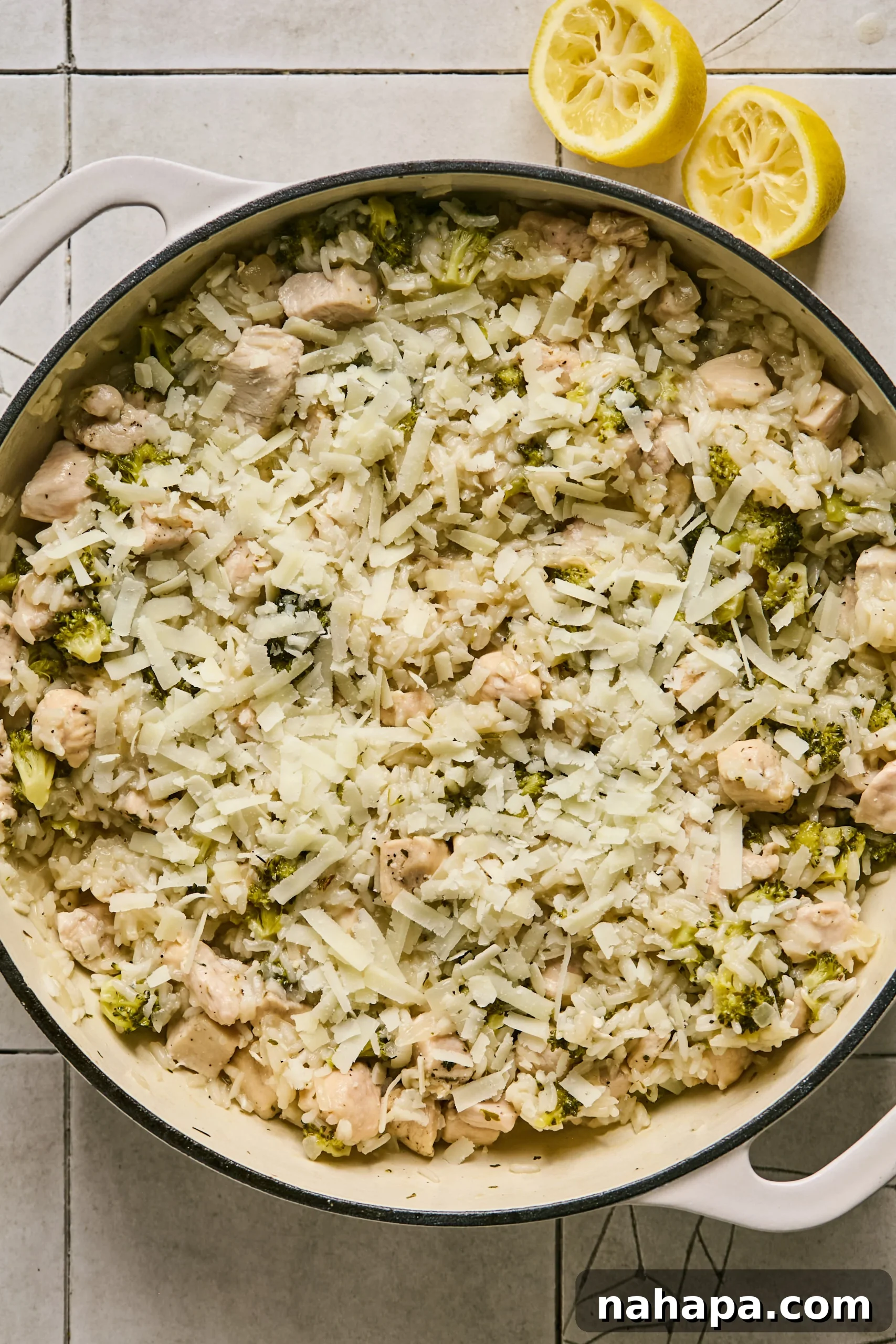 Shredded goat cheddar cheese being added over the cooked broccoli, rice, and chicken mixture in the pot.