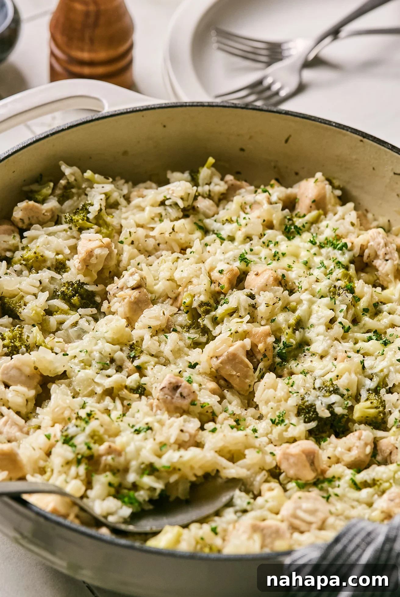 Delicious one-pot broccoli cheddar chicken and rice, garnished with fresh parsley, served in a rustic pot.