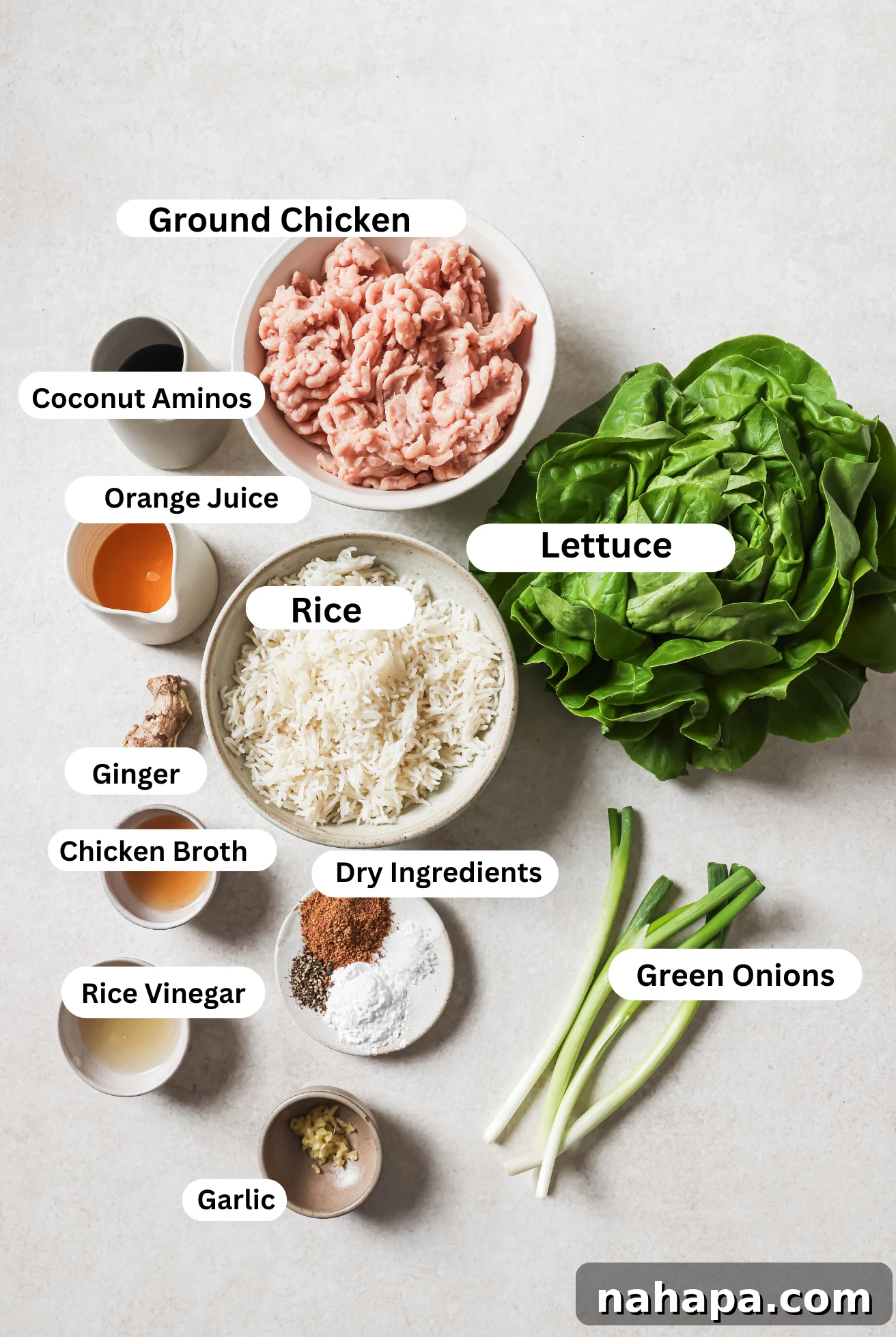 All the fresh ingredients laid out on a clean surface, including orange juice, coconut aminos, ground chicken, garlic, ginger, and lettuce leaves, for making orange ground chicken lettuce cups.