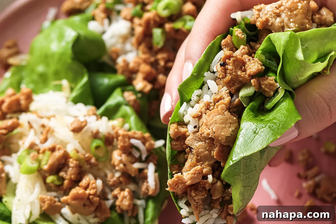 A hand holding a perfectly assembled orange ground chicken lettuce cup, filled with rice and chicken, ready to be eaten.