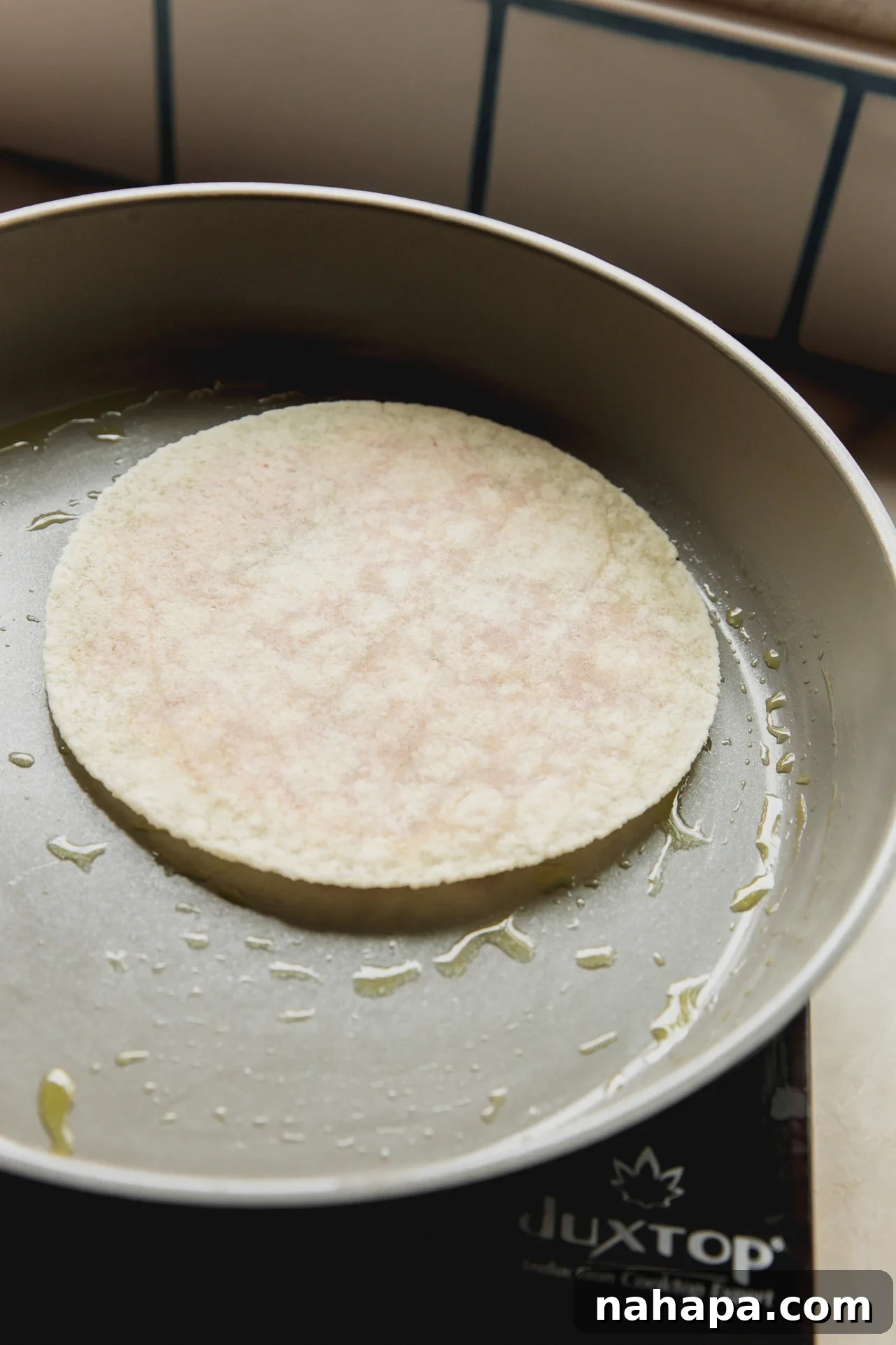 A chicken parm taco cooking in a pan with the chicken side down, sizzling.