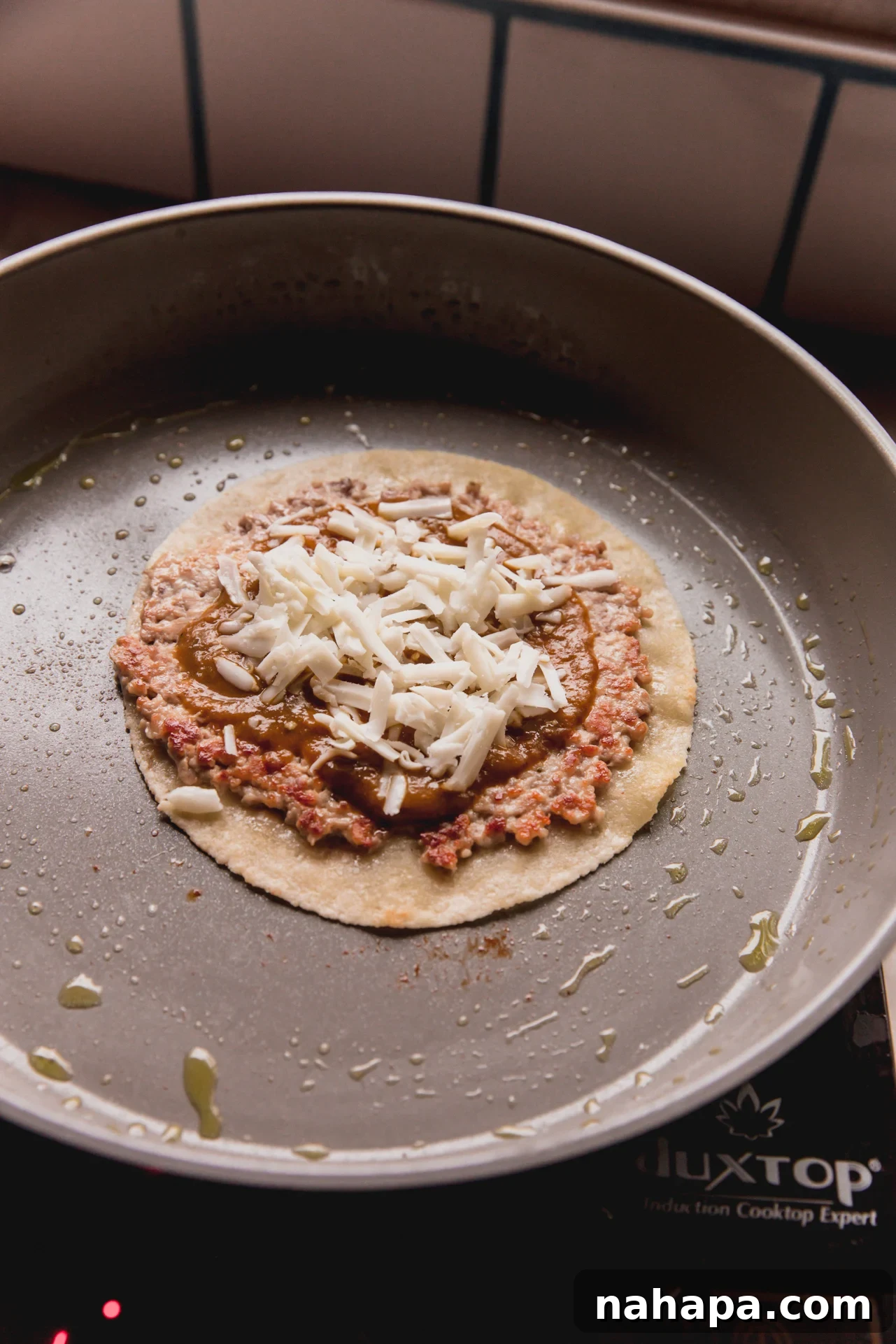 A cooked chicken parm smash burger taco in a pan, topped with pasta sauce and shredded cheese.