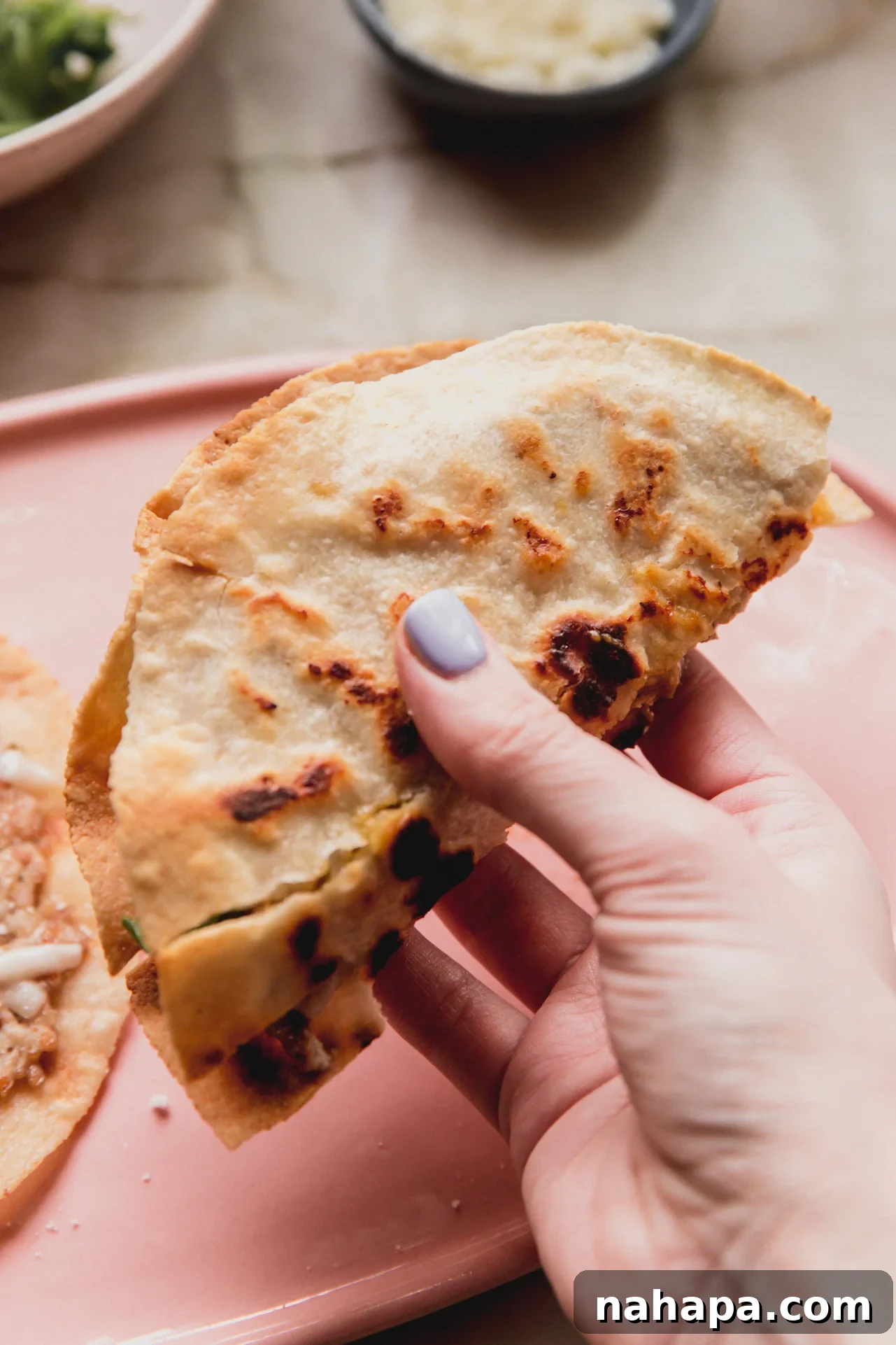 A hand holding a folded chicken parm smash burger taco, ready to be eaten, showing the crispy tortilla and melted cheese.