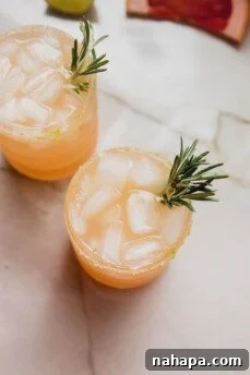 Two finished grapefruit paloma mocktails, garnished with fresh rosemary, ready to be served.