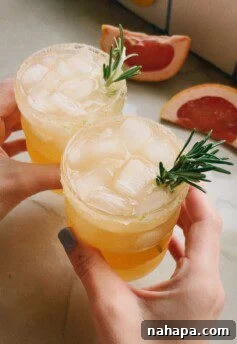 Two hands clinking glasses of grapefruit paloma mocktails in a cheerful toast, symbolizing shared joy.