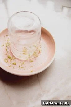 Glass rim being dipped into a mixture of lime zest and sweetener for a flavorful coating.