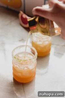 Paloma mocktail being poured from a shaker into an ice-filled glass with a prepared rim.