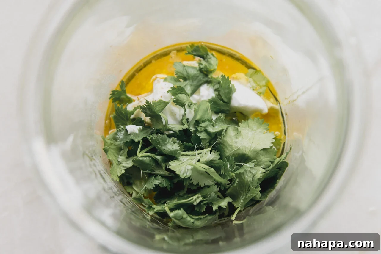 All the vibrant ingredients for homemade taco salad dressing, including creamy coconut yogurt, fresh cilantro, and lime, neatly arranged in a tall glass jar before blending.