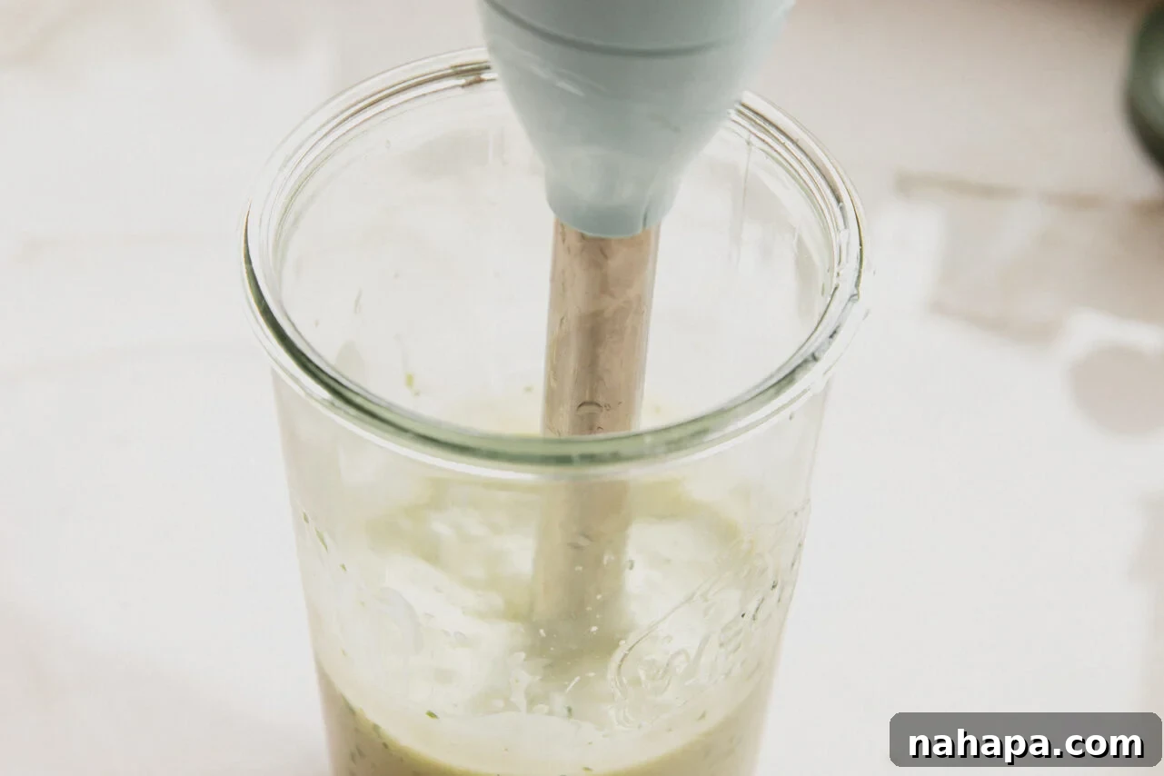 An immersion blender actively blending all the colorful ingredients within a glass jar, transforming them into a smooth, creamy homemade taco salad dressing.