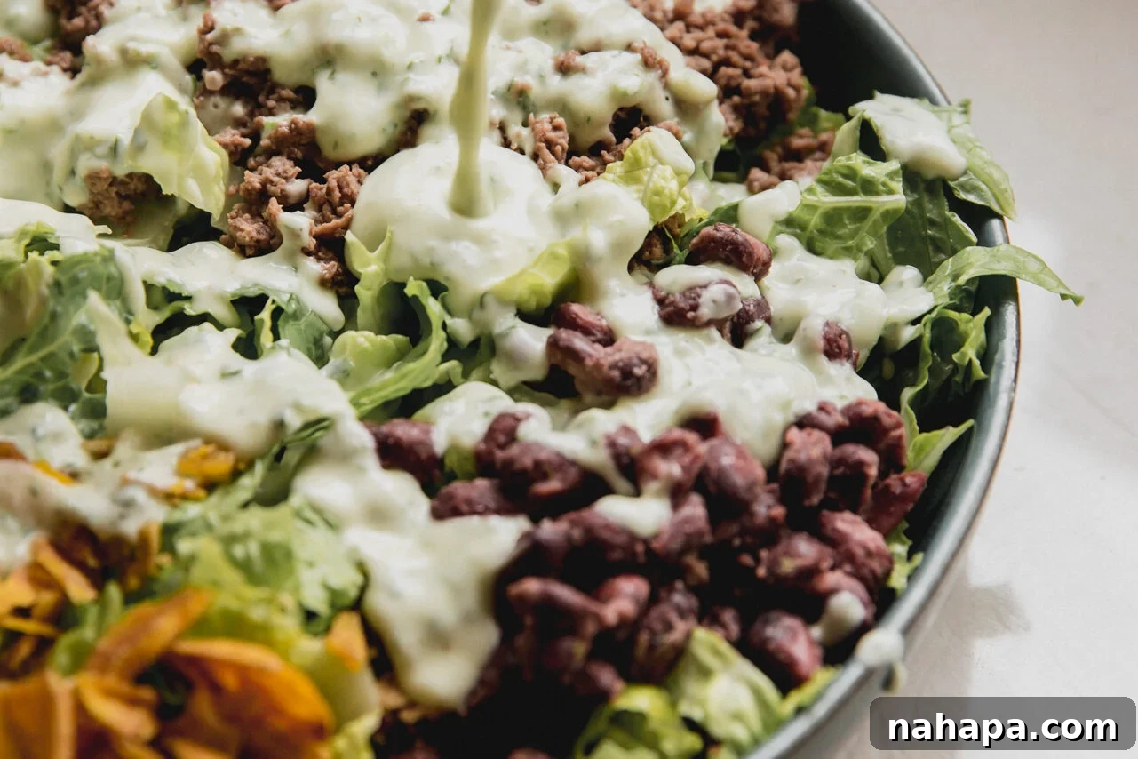 A stream of rich, creamy homemade taco salad dressing gracefully pouring from a glass jar onto a vibrant, fully-loaded taco salad, ready to be enjoyed.