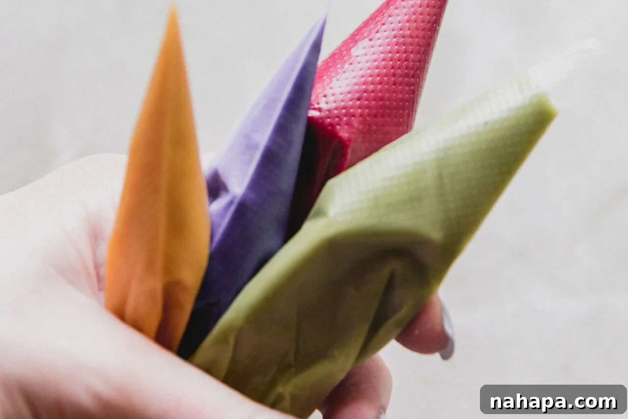Four piping bags, each filled with a different colored icing mixture, with small tips cut off.