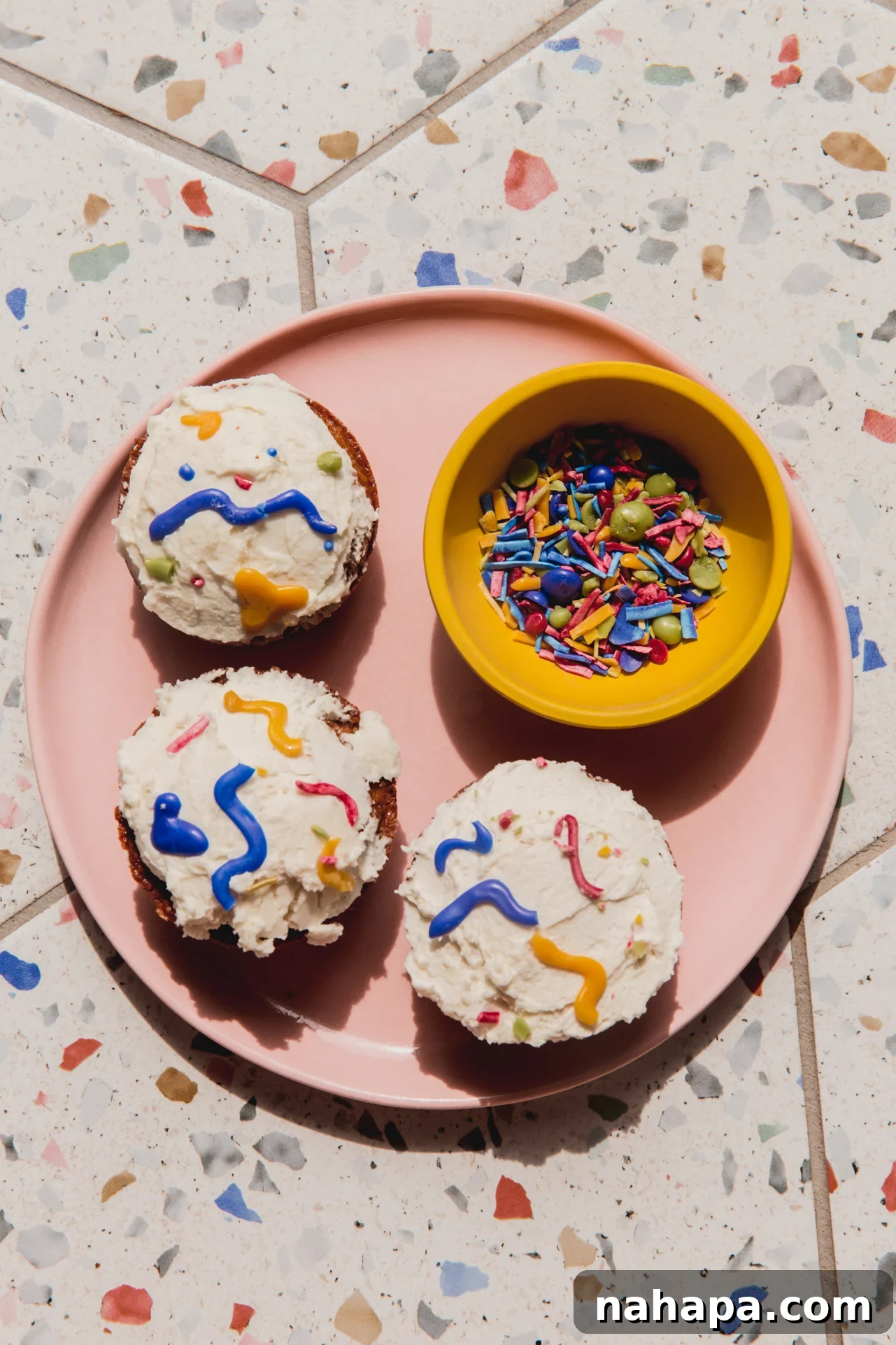 A beautiful plate of cupcakes adorned with colorful homemade sprinkles, alongside a small bowl of the sprinkles.