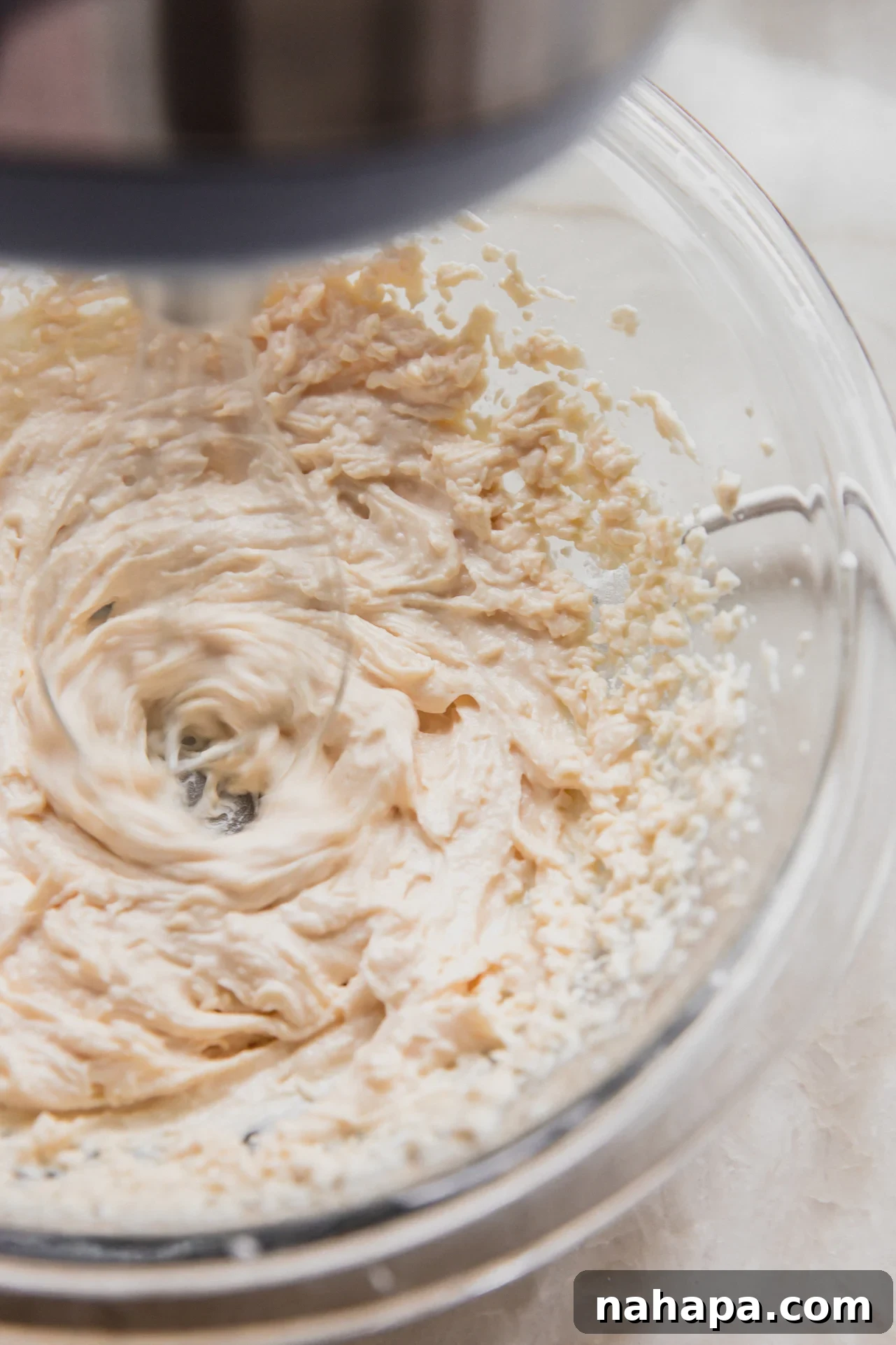 The cannoli cream being mixed by an electric hand mixer in a bowl, showing its developing creamy texture.