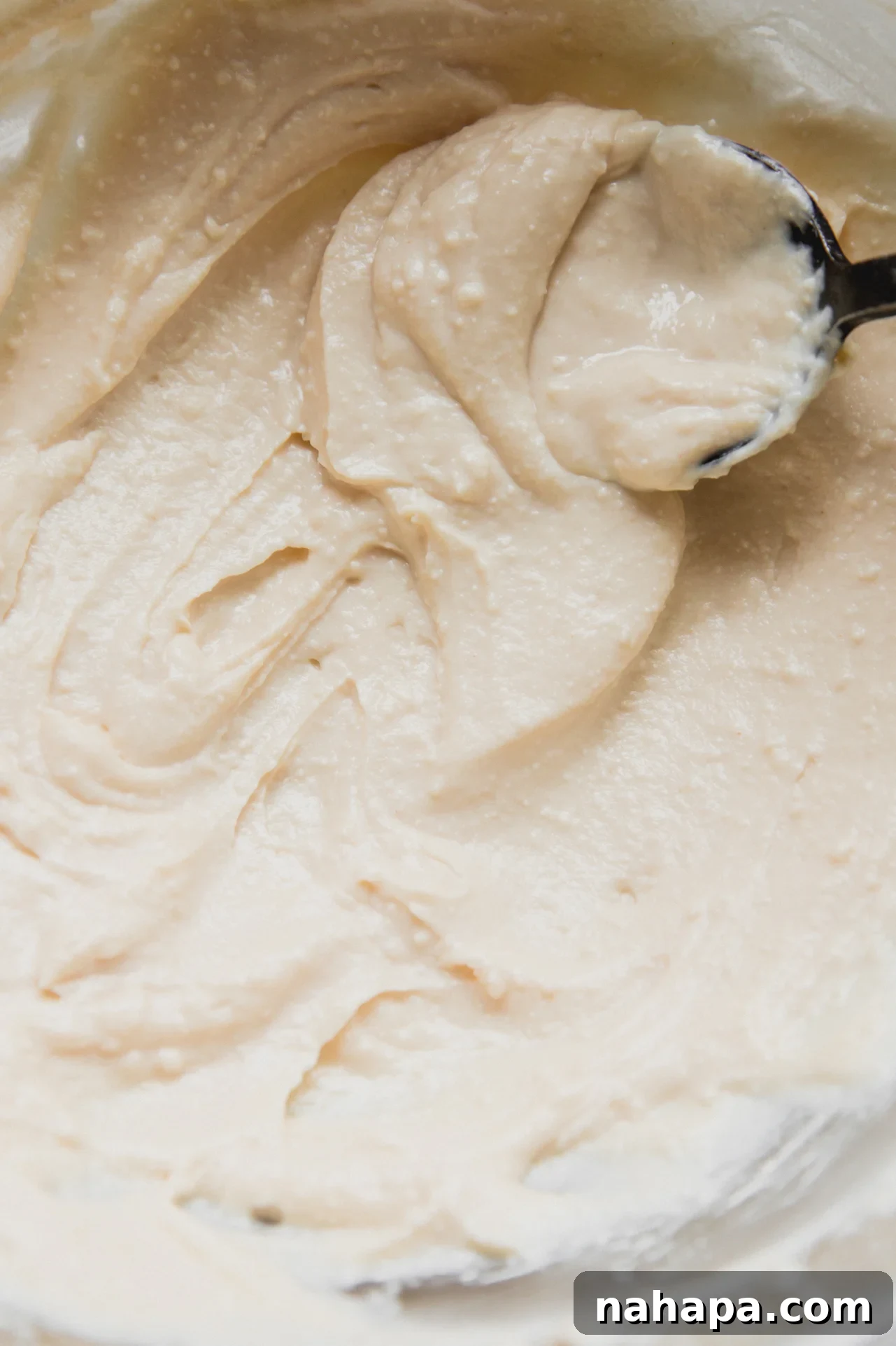 A spoon smoothing the freshly mixed cannoli cream, showcasing its light and airy texture.