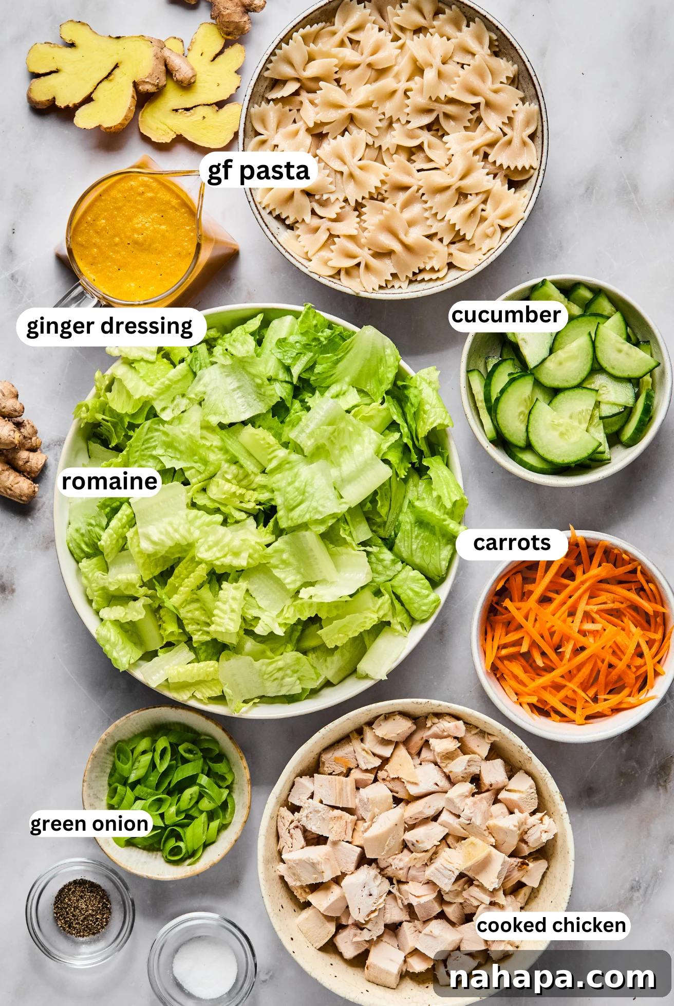 Separated bowls showcasing the fresh ingredients for Japanese Ginger Pasta Salad: gluten-free pasta, chopped romaine, sliced cucumber, shredded carrots, and cooked chicken.