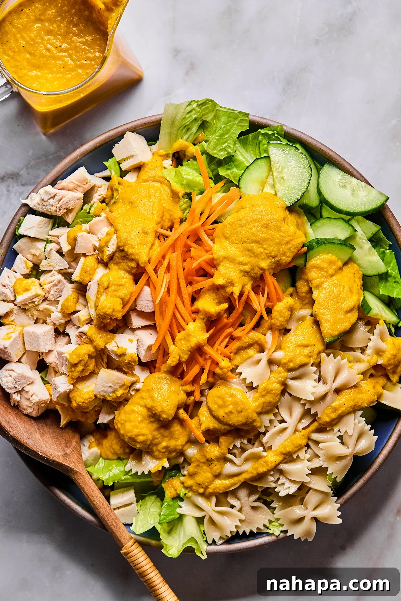 A large salad bowl containing pasta, vegetables, and chicken, with the Japanese Ginger Dressing being poured over the top.