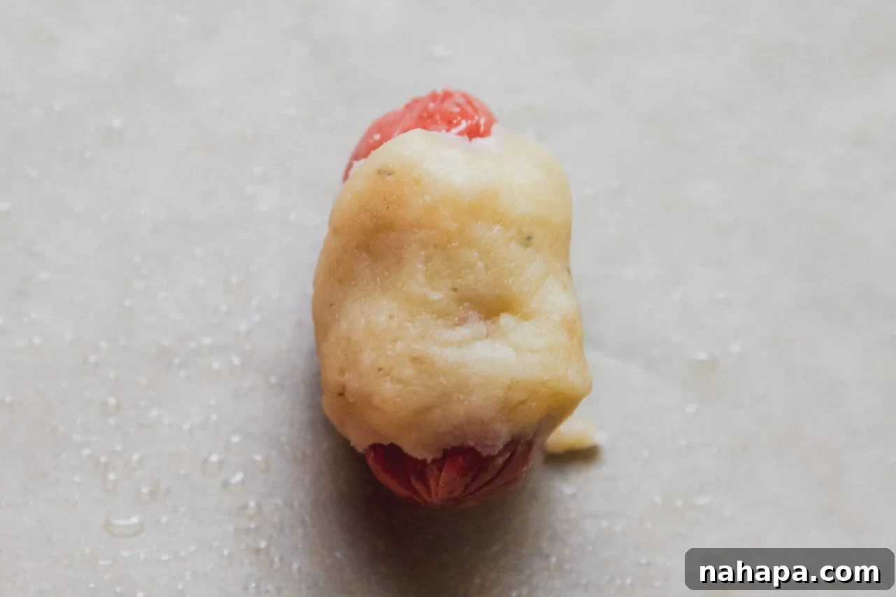 Mini hot dog partially wrapped in gluten-free dough, with ends exposed.
