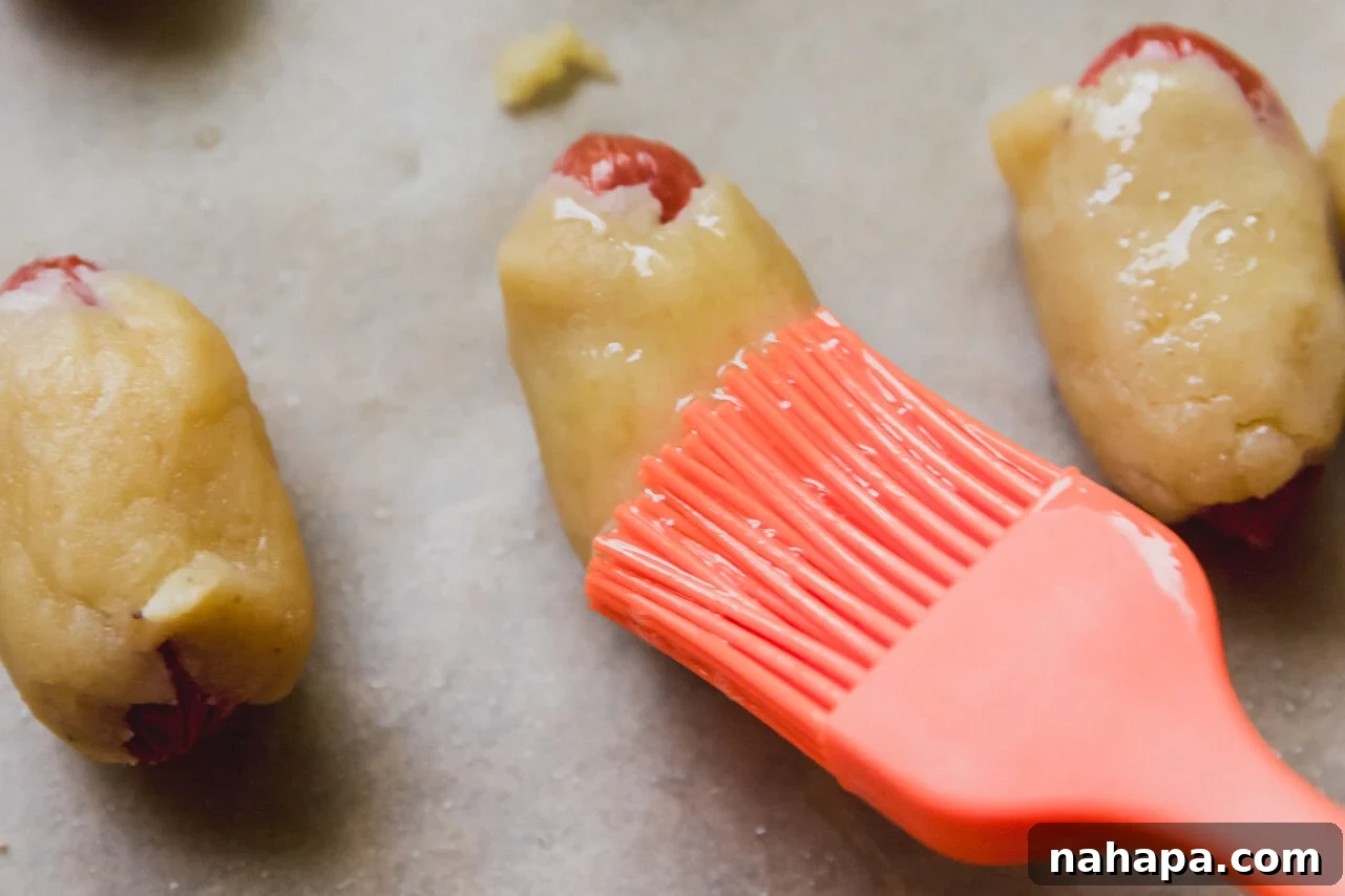 Pigs in a blanket being brushed with egg wash and sprinkled with bagel seasoning.