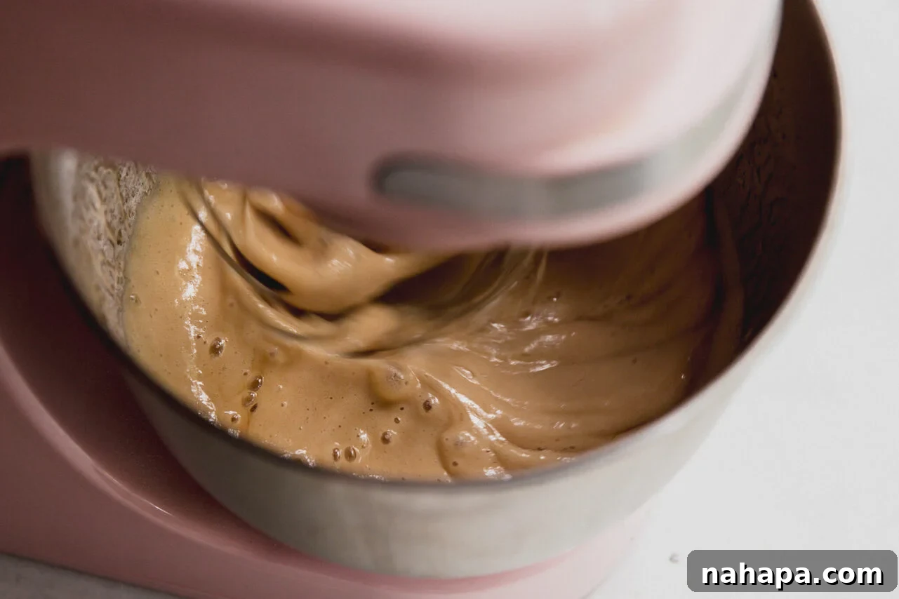Blushing Berry Mallow Fluff 6 A stand mixer in action, with the whisk attachment vigorously mixing the gradually added hot honey syrup, beginning the transformation into marshmallow fluff.