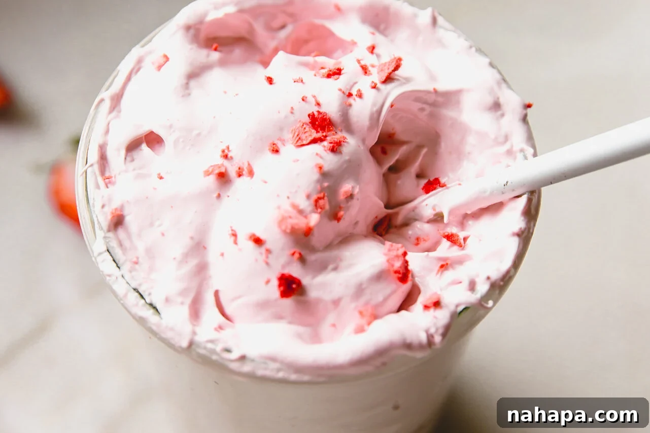 Blushing Berry Mallow Fluff 9 A spoon gracefully dipping into a jar of homemade strawberry marshmallow fluff, revealing its soft, airy texture and inviting pink color, ready to be enjoyed.