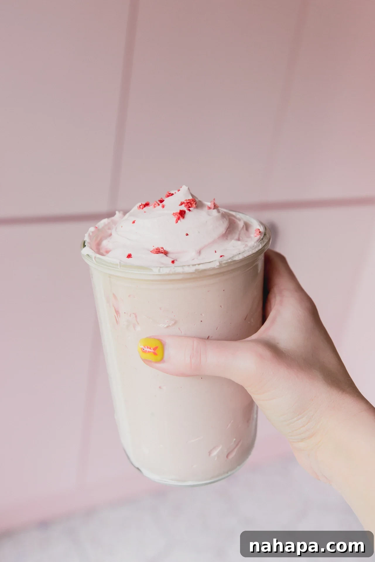 Blushing Berry Mallow Fluff 10 A hand gently holding a glass jar filled with vibrant pink homemade strawberry marshmallow fluff, ready to be enjoyed.