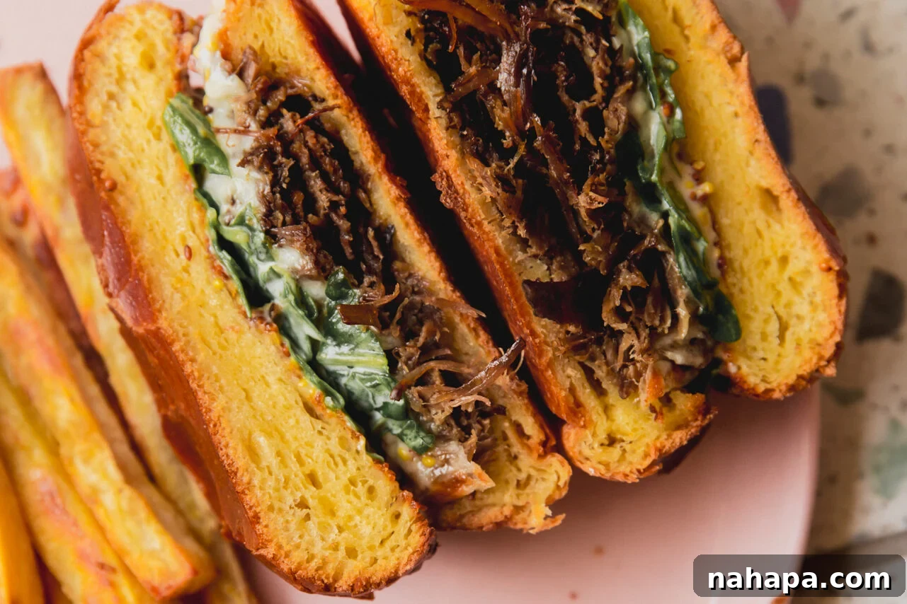 A finished slow cooker pot roast sandwich, freshly assembled and cut in half, revealing all its delicious layers.